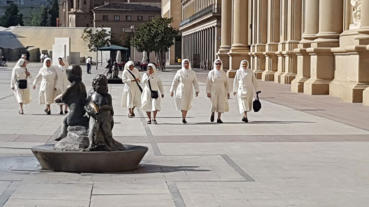 Un grupo de monjas se desplaza con serenidad a través de la amplia extensión de la Plaza del Pilar